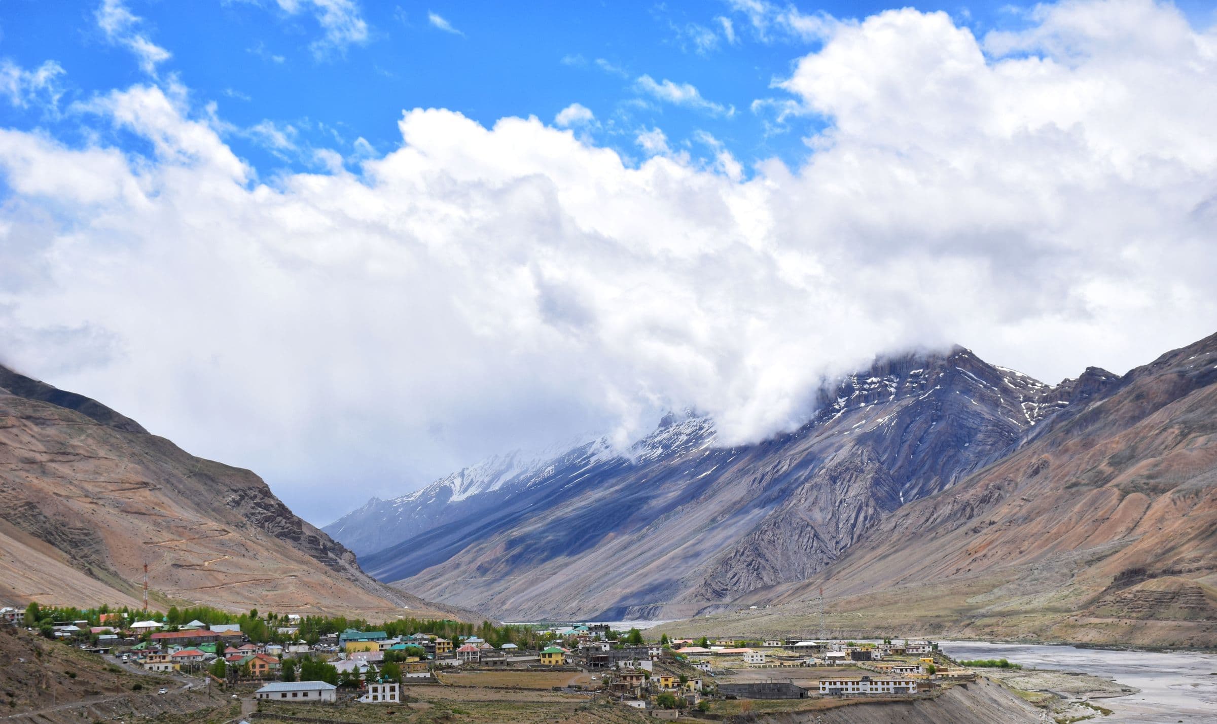 A wide Himalayan valley town beneath snow peaks and rolling cloud